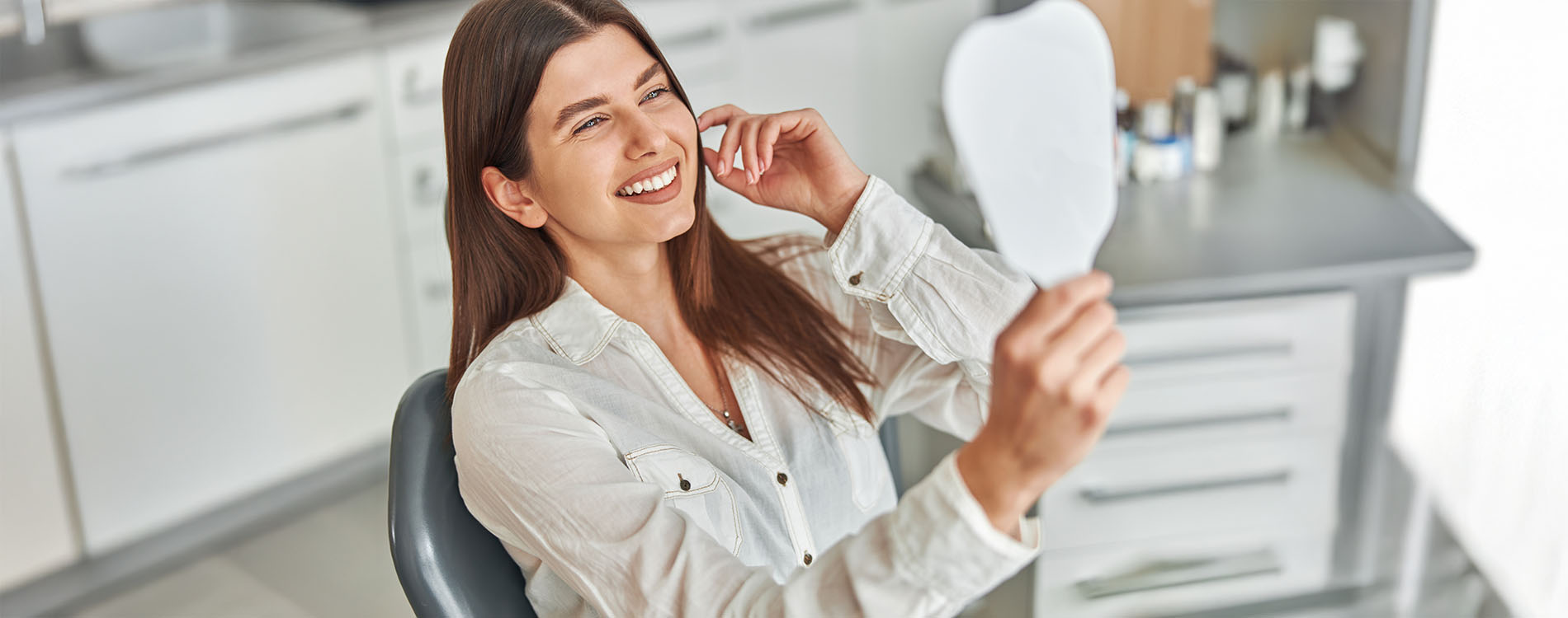 A woman sitting at a desk with her hand over her mouth, smiling at the camera while holding a phone.