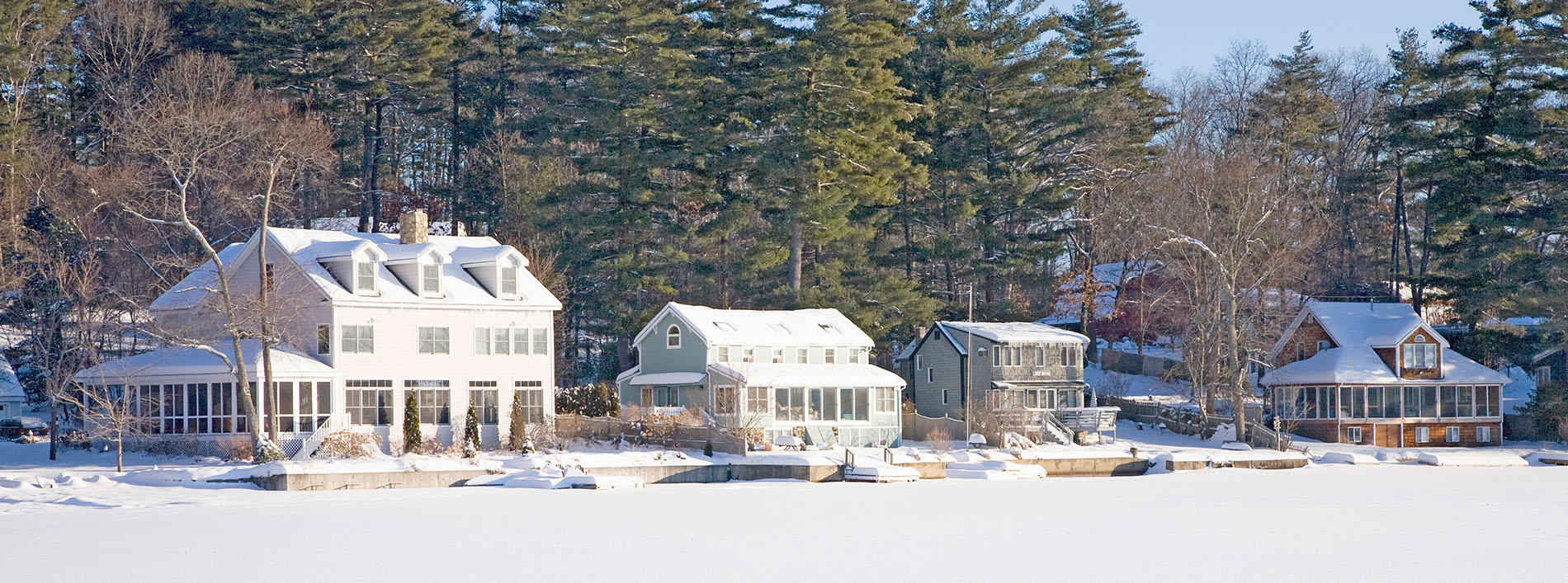 The image shows a snowy landscape featuring a two-story house with visible snow on its roof and surrounding areas, including trees and grass.