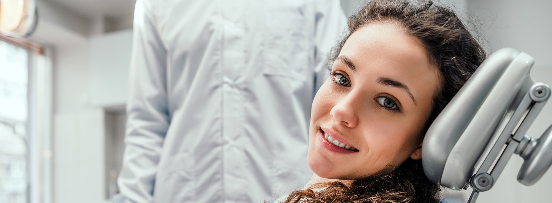 A woman sitting in a dental chair with a smile on her face looking at the camera.
