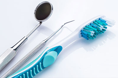 The image features a collection of dental care items including a toothbrush with blue bristles, a pair of silver scissors, and a metal dental tool, all set against a white background.