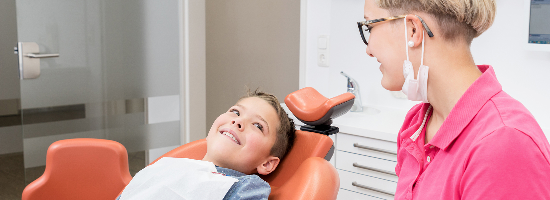 A young child receiving dental care with a smiling dental professional standing behind them.