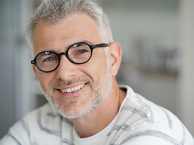 A man with grey hair, glasses, and a beard is smiling at the camera.